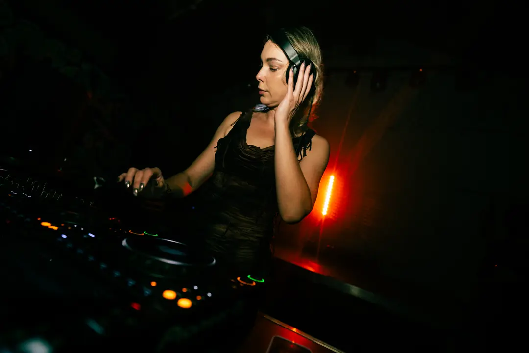 Anastasia Kristensen cueing a track with one hand on the CDJ and the other holding a headphone to her ear