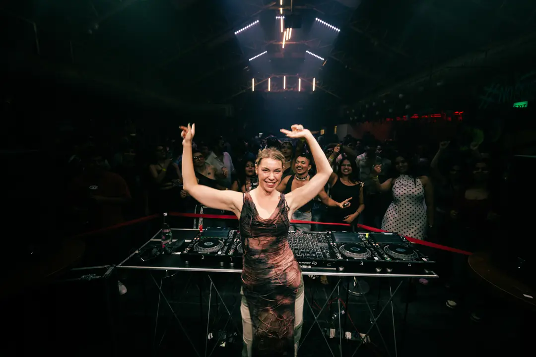 Anastasia Kristensen facing the camera with both arms raised, the crowd dancing behind the booth