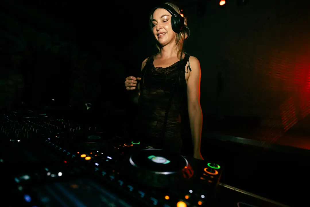 Anastasia Kristensen smiling with her eyes closed behind the decks, one hand at the strap of her dress