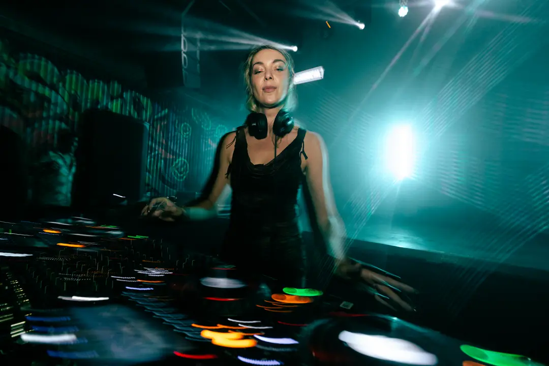 Anastasia Kristensen reaching across the decks, headphones around her neck, a white beam flaring behind her